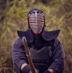 Portrait of kendoka man in the forest holding the sinai-sword.  Kendo is the Japanese martial art of sword fighting