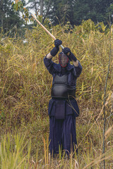 Full-length portrait of kendoka man in the forest holding the sinai-sword.  Kendo is the Japanese martial art of sword fighting