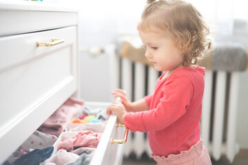 toddler girl arranges clothes and close drawer at home - obrazy, fototapety, plakaty