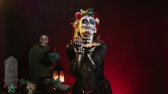 Goddess of death blowing air kisses in studio, acting flirty and romantic with cavalera catrina halloween costume. Doing kissy face with skull body art to celebrate day of teh dead holiday.