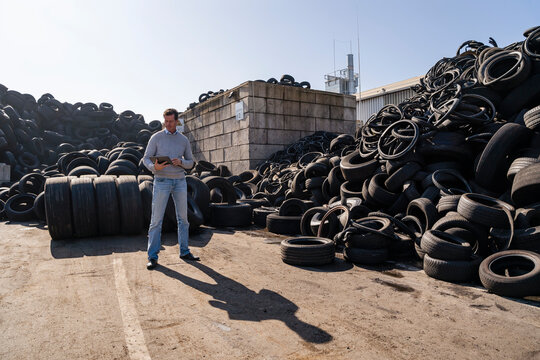 Mature businessman using tablet PC standing in front of rubber tires