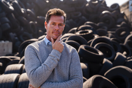 Mature businessman with hand on chin standing in front of rubber tires