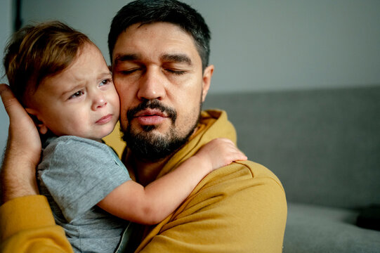 Father hugging crying son in living room at home