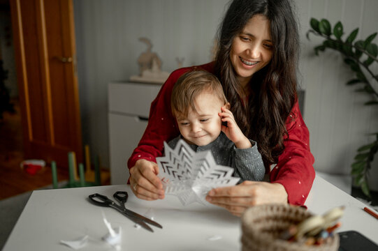 Happy Mother And Boy Making Paper Snowflakes At Home