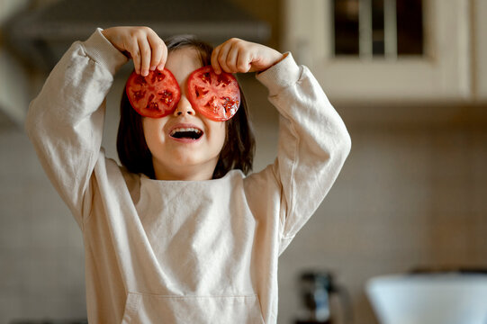 Happy boy holding tomato slices over eyes in kitchen at home