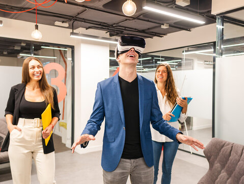 Happy businessman wearing VR glasses with colleagues in background at office