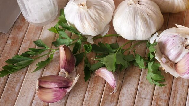 Unpeeled spicy garlic cloves and sprigs of fresh aromatic parsley on wooden cutting board. Cooking ingredients. Traditional condiments 