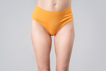 Skinny woman in orange panties on gray background, slim female thighs - obrazy, fototapety, plakaty