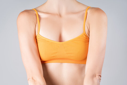 Woman in yellow top bra on gray background, small female breasts