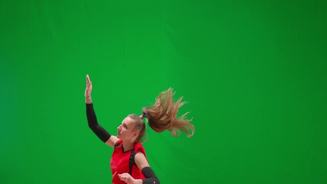 Young female volleyball player jumping and hitting the ball on green screen. Female athlete in red uniform hits the ball with her hand. Volleyball game. Putting the ball into play, serving the player.