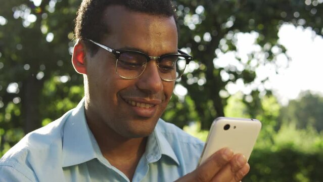 Multiethnic pretty man in glasses smiling texting in messenger app on smartphone