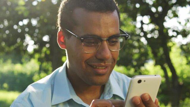 Positive excited multiethnic man making yes gesture looking at smartphone display, betting on sport and winning, participating at online auction, buying shares at bargain price, e-commerce