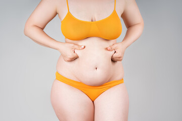 Fat woman in orange underwear on gray background, overweight female body