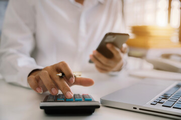 Investors working using calculator to calculate with smartphone, laptop the tax of static in...