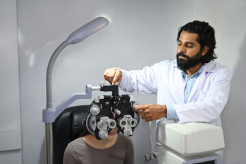 Image of Indian ophthalmologist using medical equipment to check up eyesight of clients in clinic