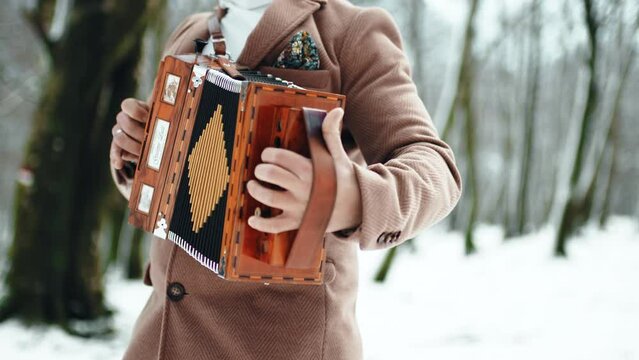 Man playing accordion into the forest during winter season