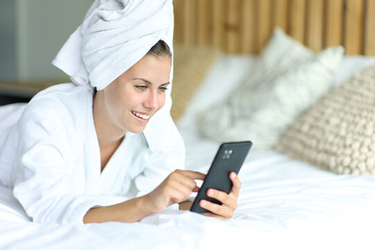 Happy teen after showering using cell phone on a bed