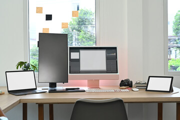 Creative office studio interior with laptop, blank screen computer, digital tablet and stationery on wooden table