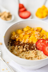 Close up view oatmeal porridge with strawberries, mango and nuts
