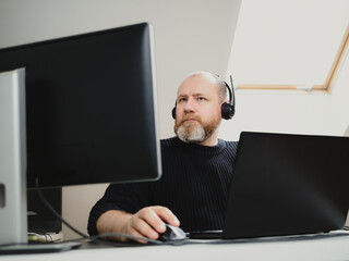 Adult man remote working on laptop and using two monitors and headphones from home