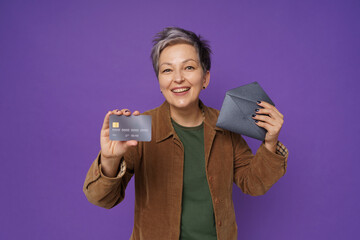 Holding credit, debit card mature woman with fancy dark envelope. Happy mature woman got her new bank debit, credit card, wearing casual isolated on purple background. Banking, financial concept