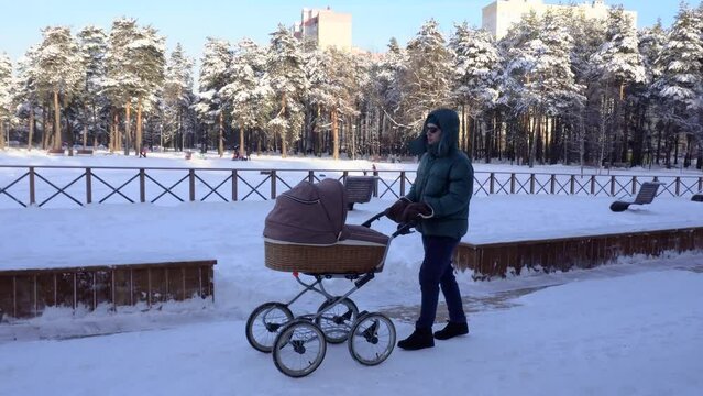 Father with the baby carriage is walking in a winter city park.