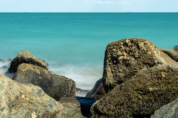 Fototapeta na wymiar Brandungswellen in Langzeitbelichtung mit Felsen am Strand und blauem Ozean