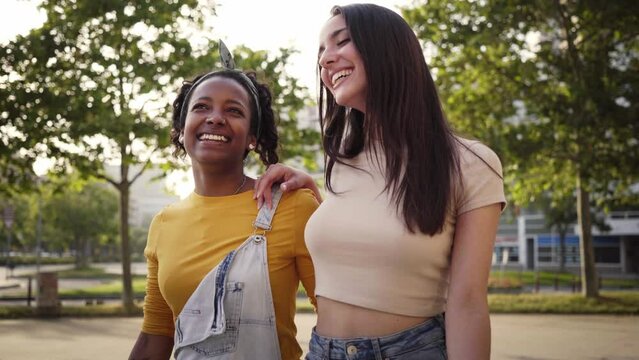 Two beautiful women laughing as they walk down the street. Female friends having fun together in the city park. A lesbian couple talk happily outside. LGBTI pride people. Girlfriends lovers.