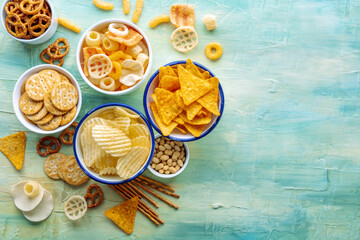 Salty snacks. Potato and tortilla chips, crackers and other appetizers in bowls, overhead flat lay shot with copy space. Party food background - obrazy, fototapety, plakaty
