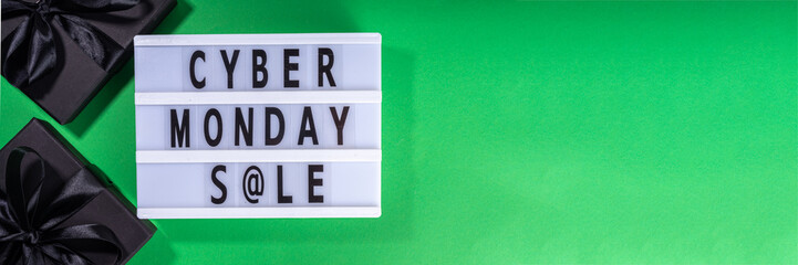 Cyber monday sale background. Simple bright green flat lay with lightbox "Cyber monday", gift boxes, shopping cart, laptop, tablet, headphones top view copy space. Online holiday shopping concept