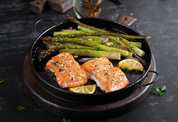 Delicious baked salmon with asparagus, lemon slices and spices on dark table.