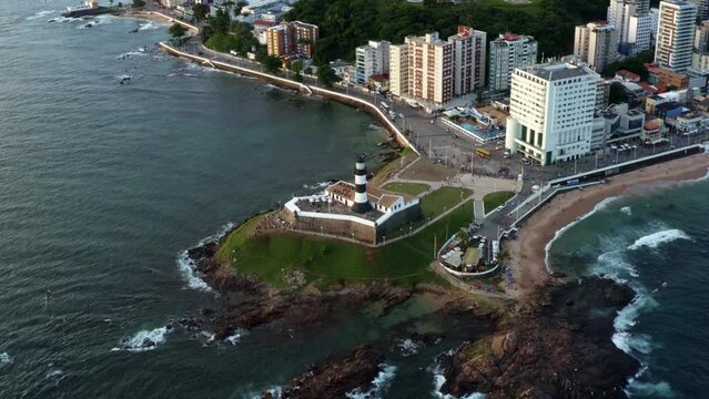 Rising and panning aerial drone shot looking down at the historical Barra or Santo Ant&ocirc;nio Lighthouse in the cultural Afro-Brazilian city of Salvador in Bahia, Brazil with crowds watching the sunset