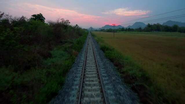 Travel by train in Thailand. View through the rear door of the car. The railroads going into the distance from the time of the red dawn. Asia Railway.
