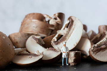 Sliced chestnut mushrooms on a slate cutting board, with a miniature scale model chef in uniform