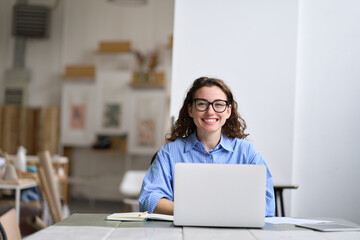 Young happy business woman company employee sitting at desk working on laptop. Smiling female...