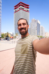 Cheerful selfie of handsome guy looking at camera smiling, standing with the city in the background.