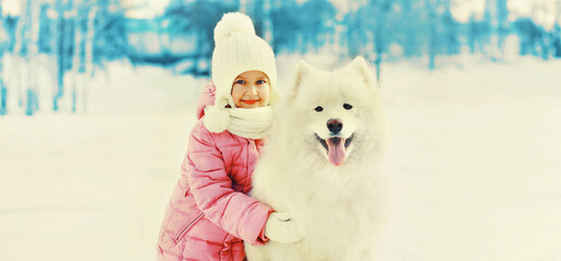 Cheerful little girl child with white Samoyed dog in winter park