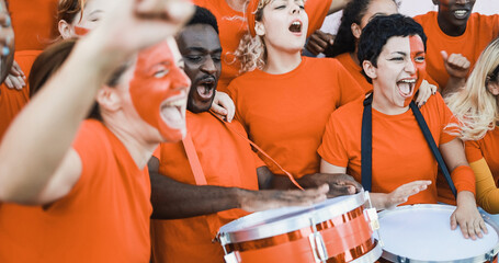 Multiracial orange sport fans screaming while supporting their team - Football supporters having...