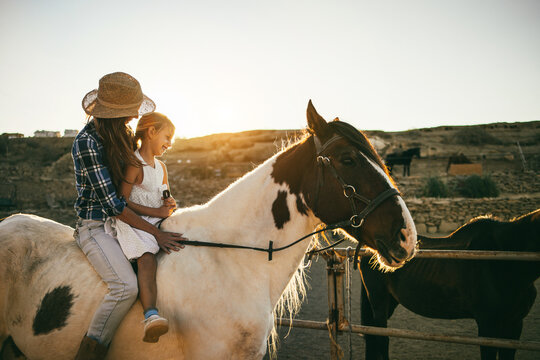 Happy mother and daughter riding a horse at sunset - Soft focus on girl face