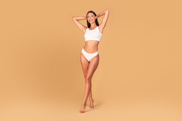 Happy slender caucasian lady posing in white underwear over beige studio background, showing her beautiful curves