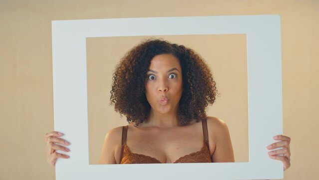 Studio shot of confident and positive woman smiling and looking through cardboard picture frame and pulling funny faces - shot in slow motion