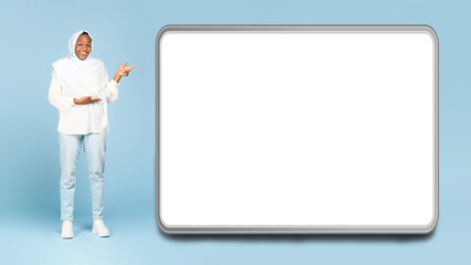 Wow, look here. Happy black muslim woman pointing at big blank device display, showing huge white empty screen