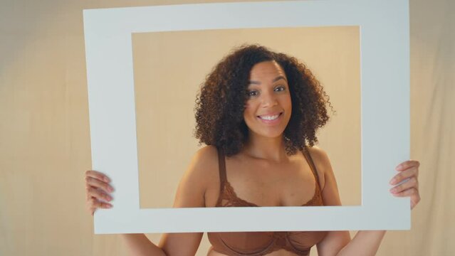 Studio shot of confident and positive woman smiling and looking through cardboard picture frame, blowing a kiss and pulling funny faces - shot in slow motion