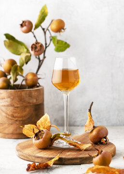 Homemade wine or liquor of medlar fruit in a small glass with fresh ripe fruits on wooden cutting board. (Mespilus germanica) Copy space.