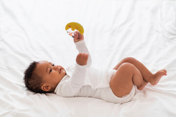 Cute Small Black Baby With Rattle Toy In Hand Relaxing In Bed