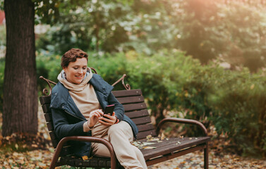 Fototapeta premium A woman in an autumn park reads messages in a smartphone