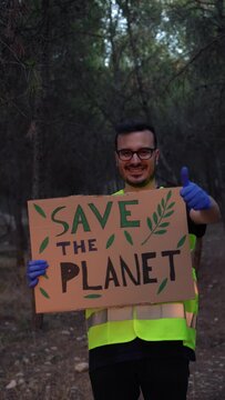 Hombre voluntario, ense&ntilde;ando una pancarta con el mensaje salva tu planeta, en la monta&ntilde;a, con expresi&oacute;n sonriente. Video vertical 4K.
