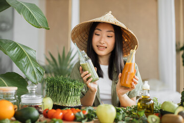 Charming young asian vegan woman preparing healthy fresh smoothie for breakfast on tropical exotic...