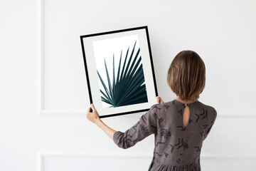 Young woman installing photo frame on white wall, Minimal photographer artist concept.