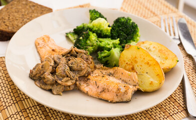 fried river trout fillet with a complex side dish of broccoli, baked potatoes and mushroom sauce